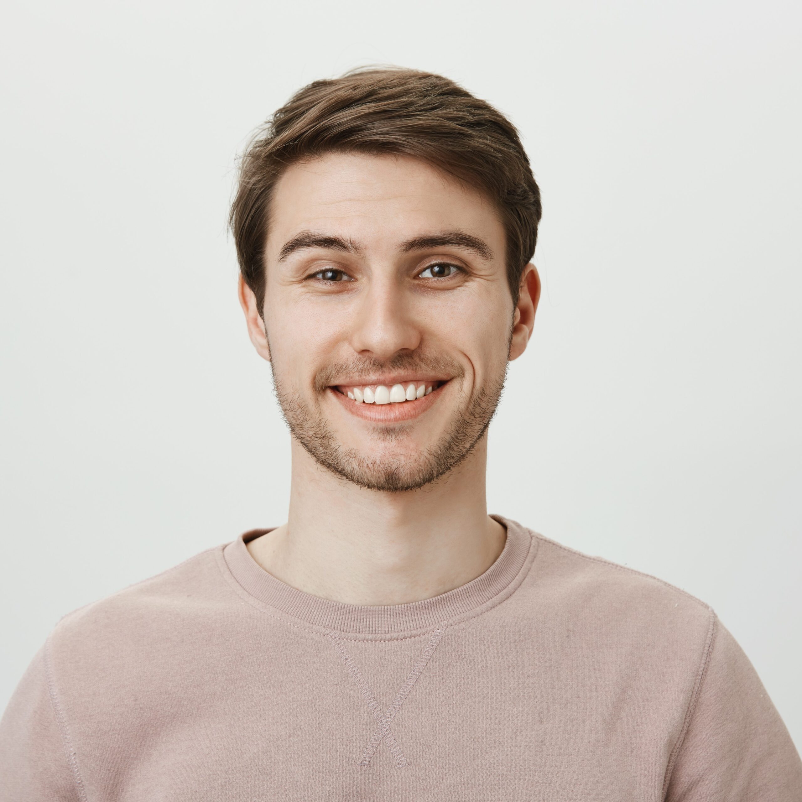 Confident attractive caucasian guy in beige pullover smiling broadly while standing against gray background, feeling self-assured while helping out customer, giving some advice about his investments.