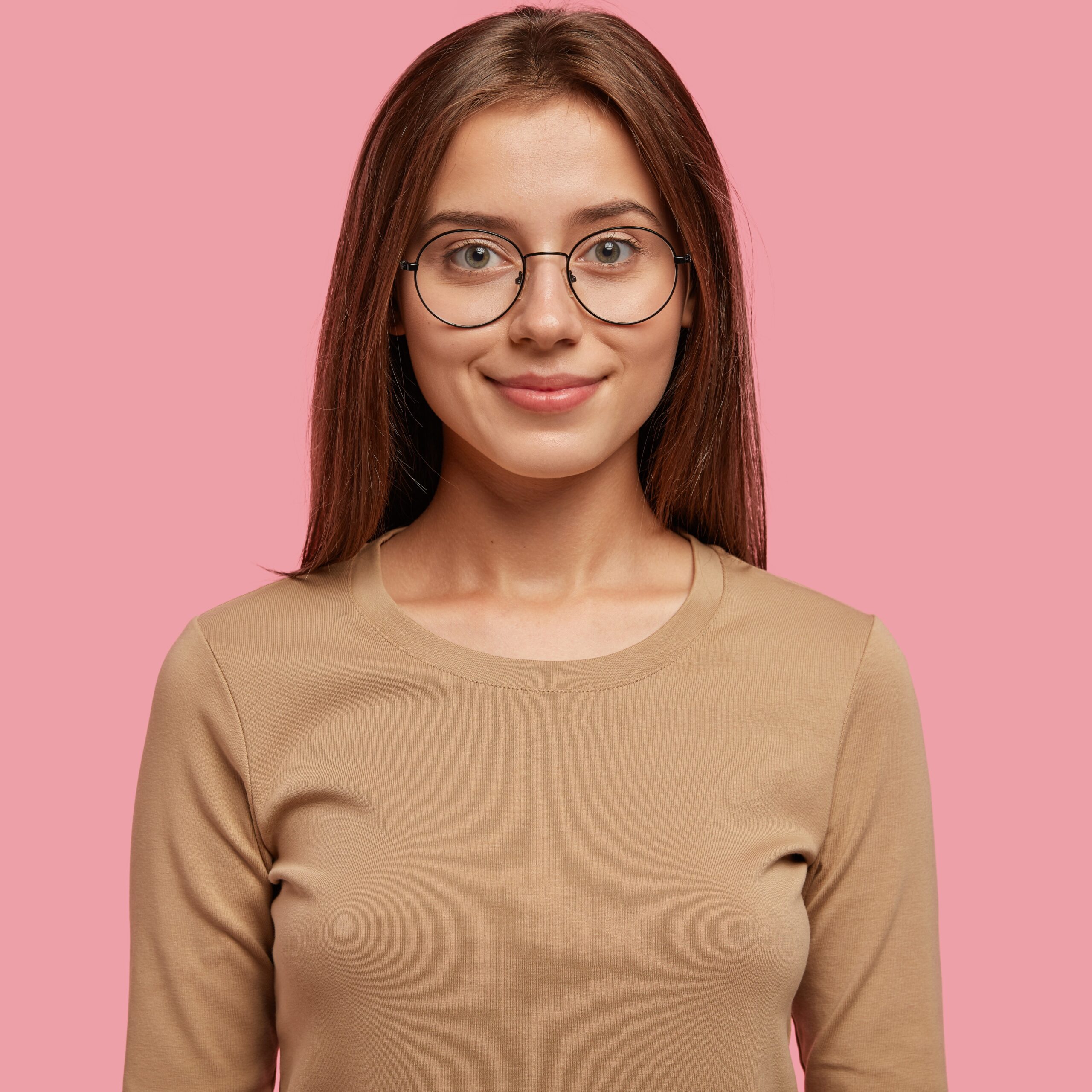 Photo of pleasant looking girl has healthy soft skin, dark staright hair, dressed in casual sweater, looks directly at camera, models against pink background. People, beauty and facial expressions
